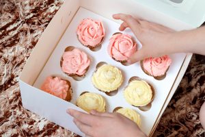 cupcakes-mit-rosa-und-gelber-creme-im-papierkasten-auf-braunem-hintergrund_81856-572