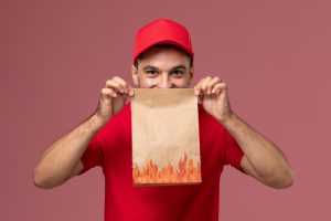 front-view-male-courier-red-uniform-cape-holding-paper-food-package-pink-wall-service-delivery-male-uniform-worker_140725-35607